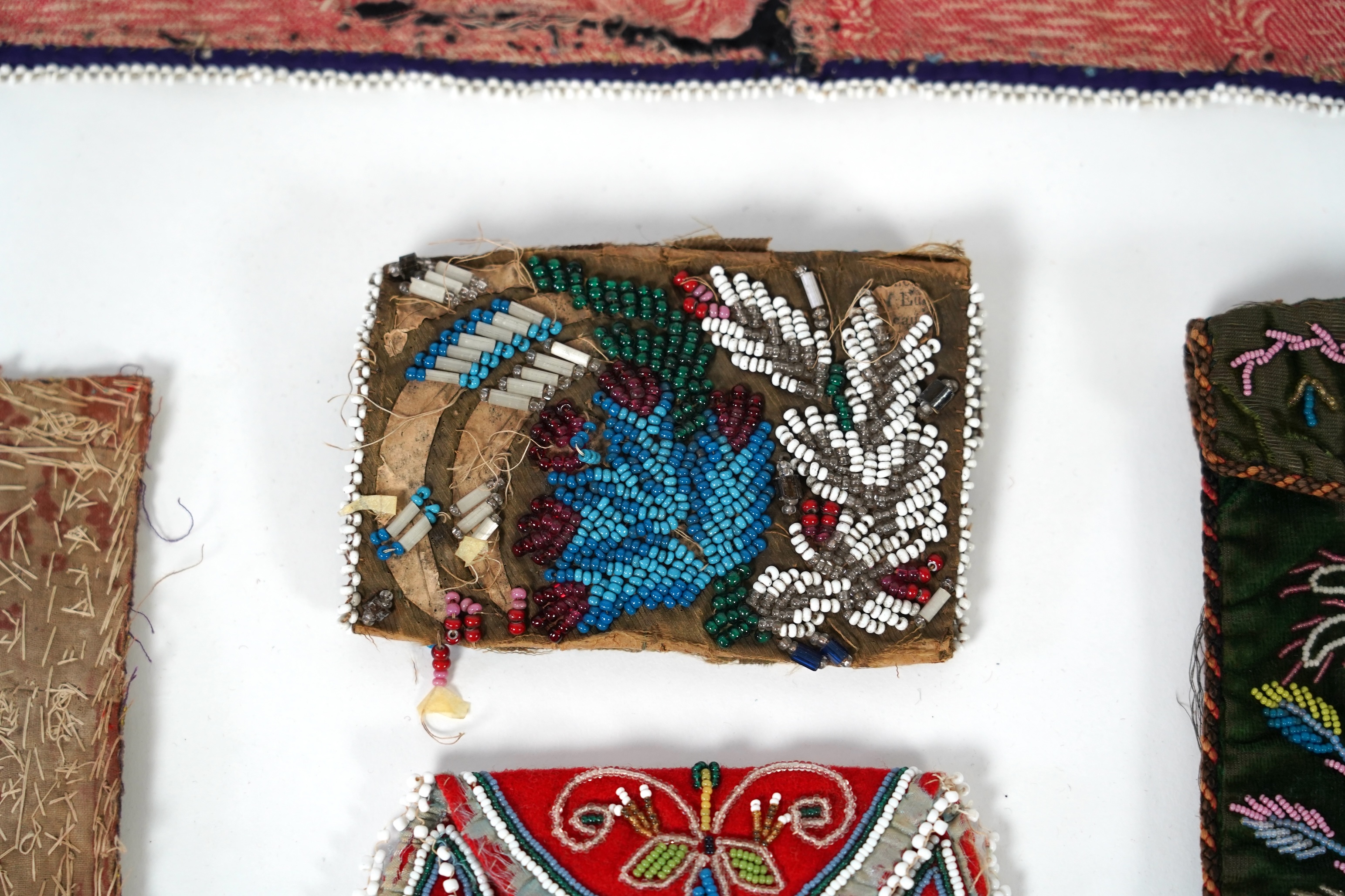 A 19th century black felt multi coloured beadwork panel, possibly North American Indian and a similar purse, a Regency fine bead worked bible bag, a similar worked belt and small panel, a red bead work purse and a small